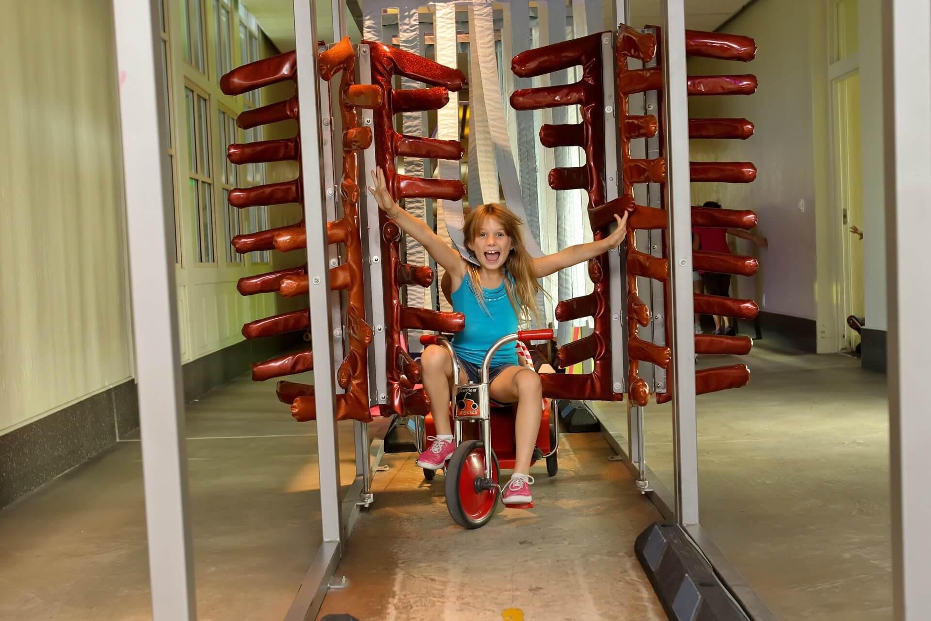 Young girl pedaling a trike through a colorful exhibit at the Children's Museum of Phoenix